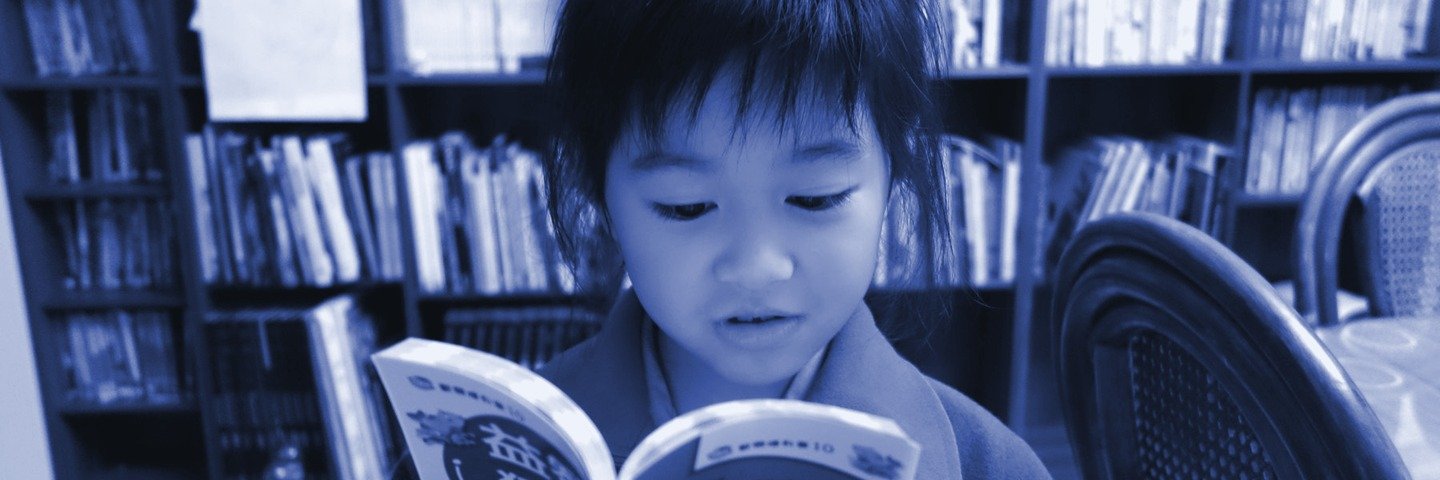 Un jeune enfant lit un livre devant des étagères de bibliothèque